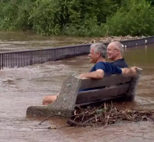 2 guys sitting on a bench in a flood 